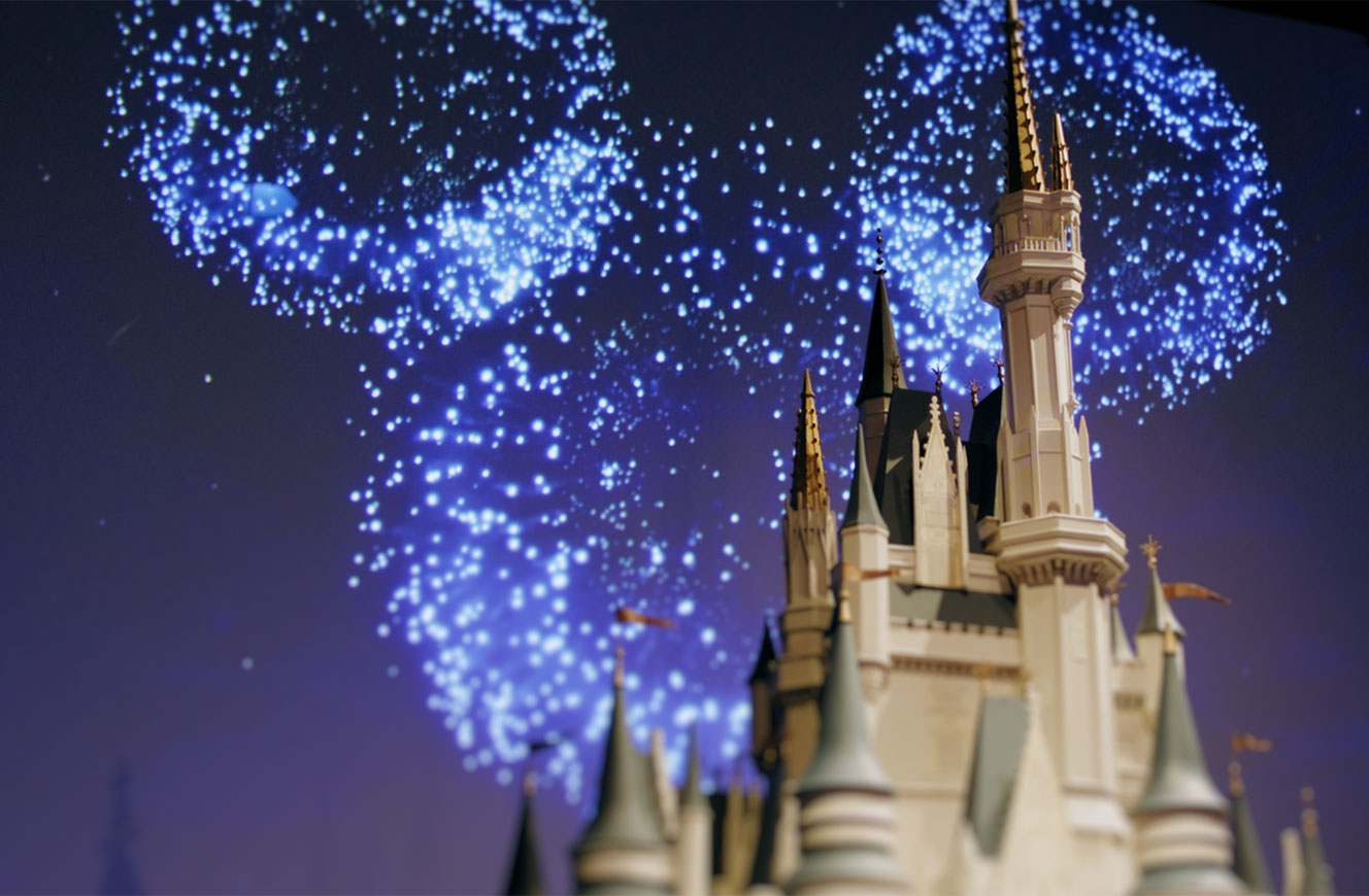 Modell des Disney-Schlosses im Vordergrund mit animierter Feuerwerksprojektion im Hintergrund – Teil der Disney 100 Ausstellung, Medieninszenierung von cocurio