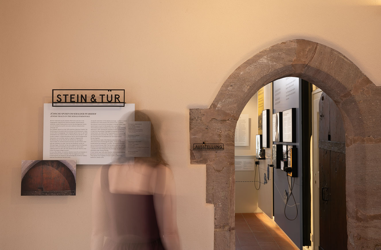 Eingangsbereich mit dem Ausstellungstitel Stein & Tür neben einem historischen Steinbogen, dahinter der Ausstellungsraum