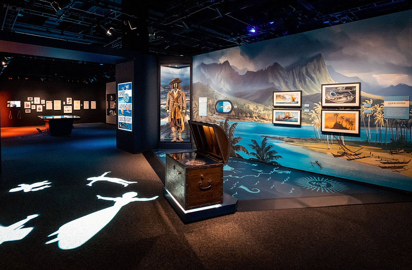 Szene aus dem Raum ‚Adventure‘ der Disney 100 Ausstellung mit Pirates-of-the-Caribbean-Mannequin vor großformatigem Hintergrunddruck – medial bespielte Flasche in der Vitrine, Medieninhalte von cocurio