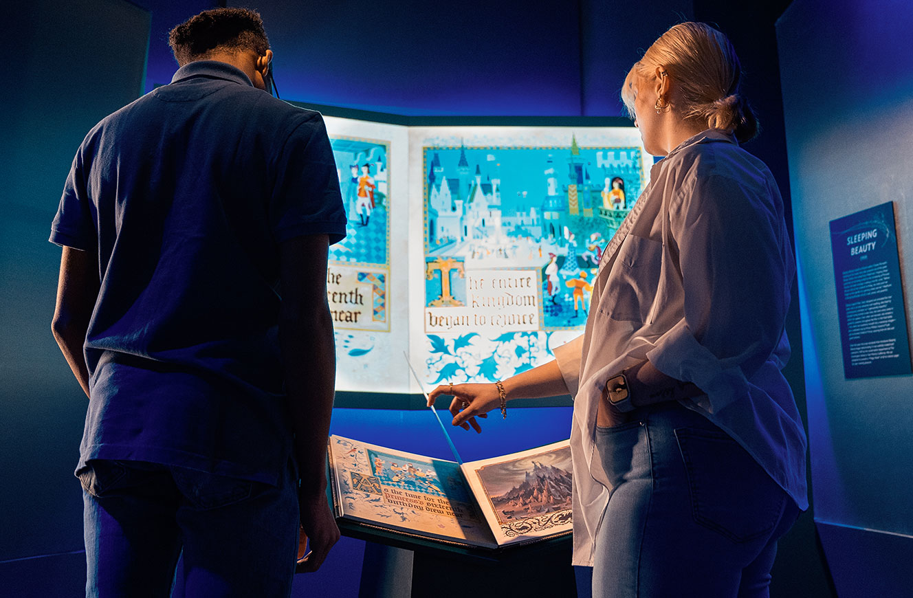 Besucher:innen interagieren mit dem Magic Book – einer animierten Medieninstallation zu Dornröschen in der Disney 100 Ausstellung, konzipiert und gestaltet von cocurio