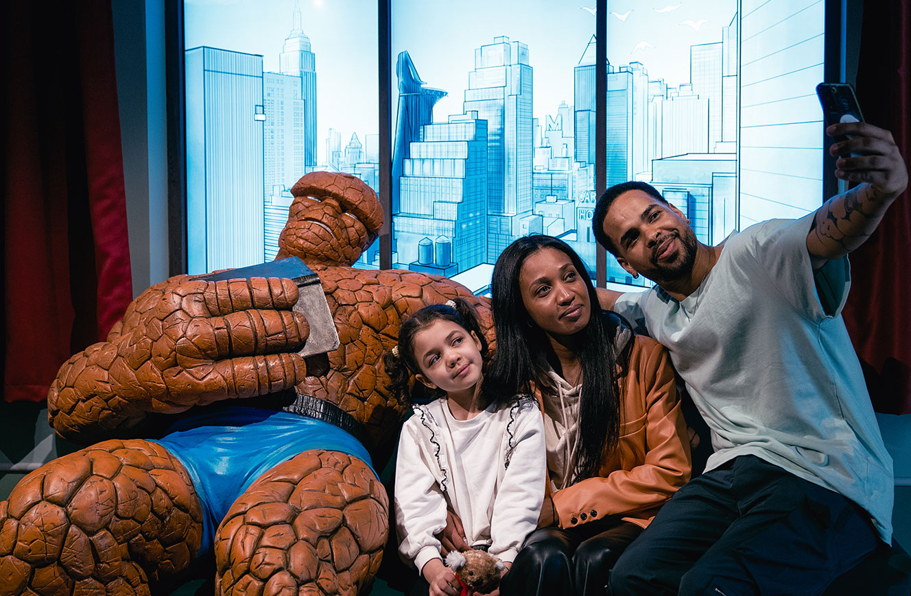 Besucherfamilie macht ein Selfie mit der Figur The Thing vor einer gezeichneten Stadtkulisse – Marvel: Universe of Super Heroes