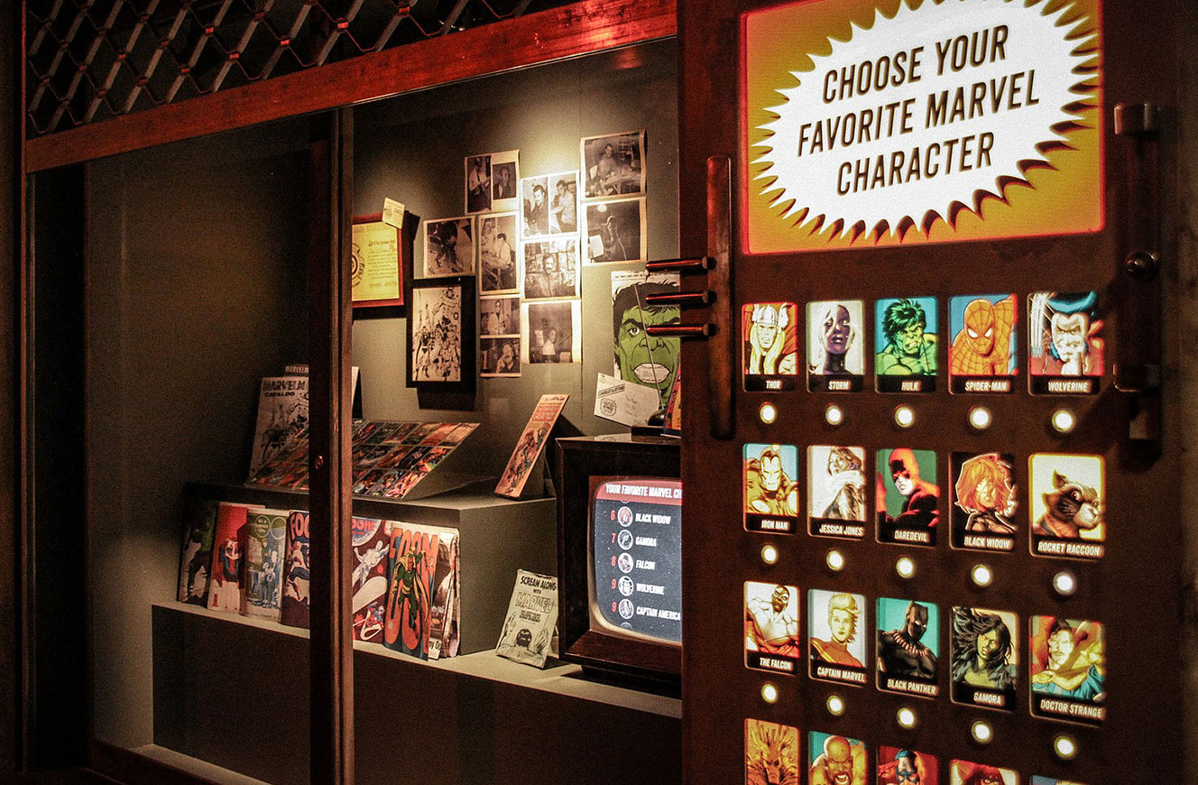 Interaktive Station „Choose your favorite Marvel character“ mit beleuchteten Auswahltasten neben einer Comic-Vitrine