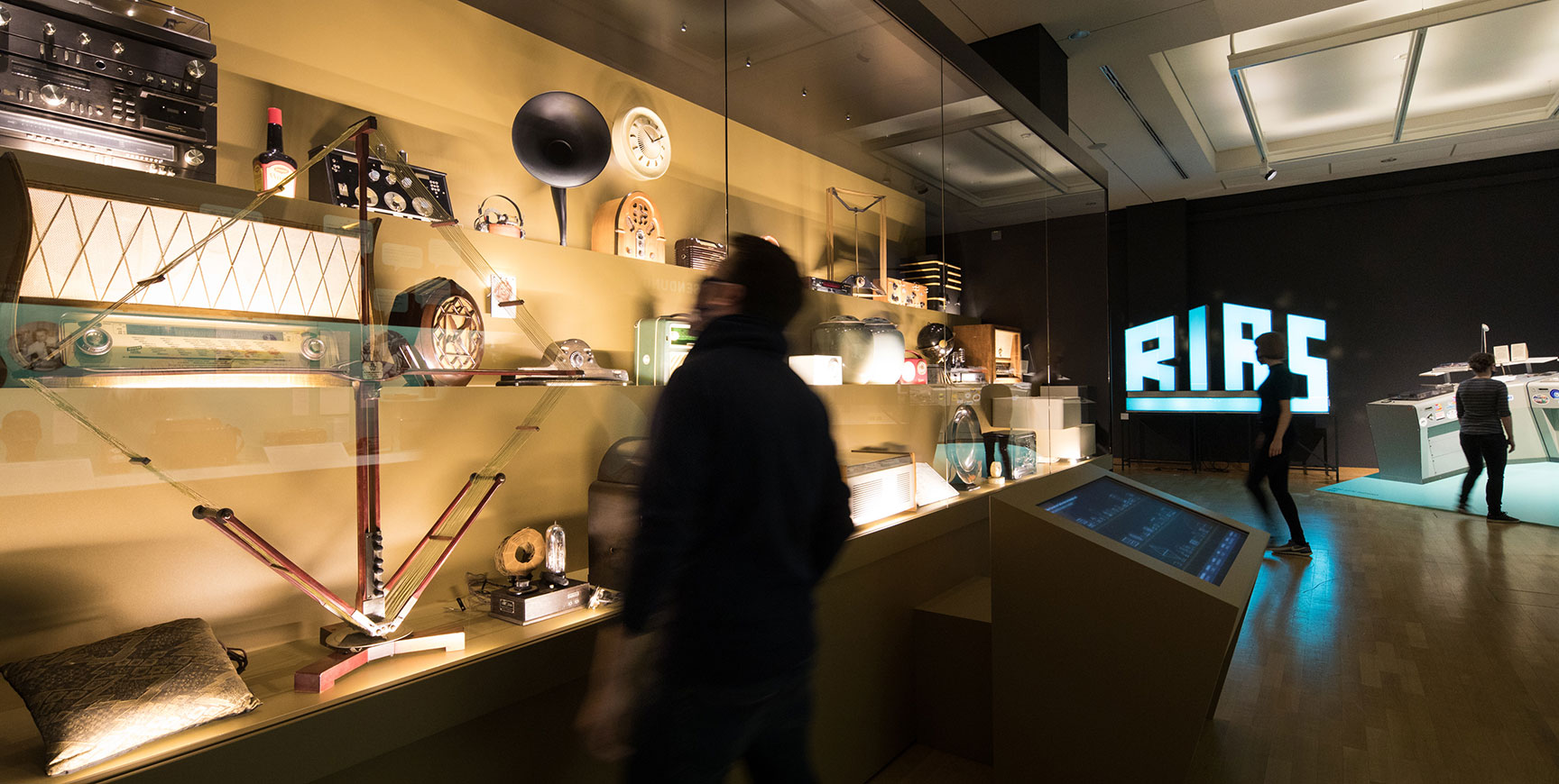 Ausstellungsraum mit Vitrine historischer Radiogeräte, Medientisch und leuchtendem RIAS-Schriftzug – On Air, 100 Jahre Radio