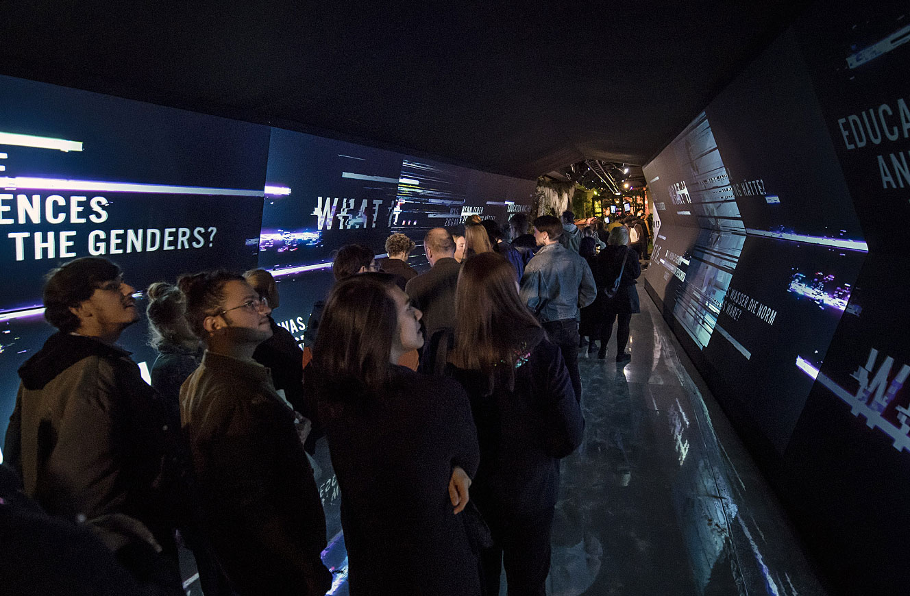 Besuchergruppe in einem dunklen Tunnel mit leuchtenden Textprojektionen an den Wänden – Medientunnel der Urban Nation Biennale