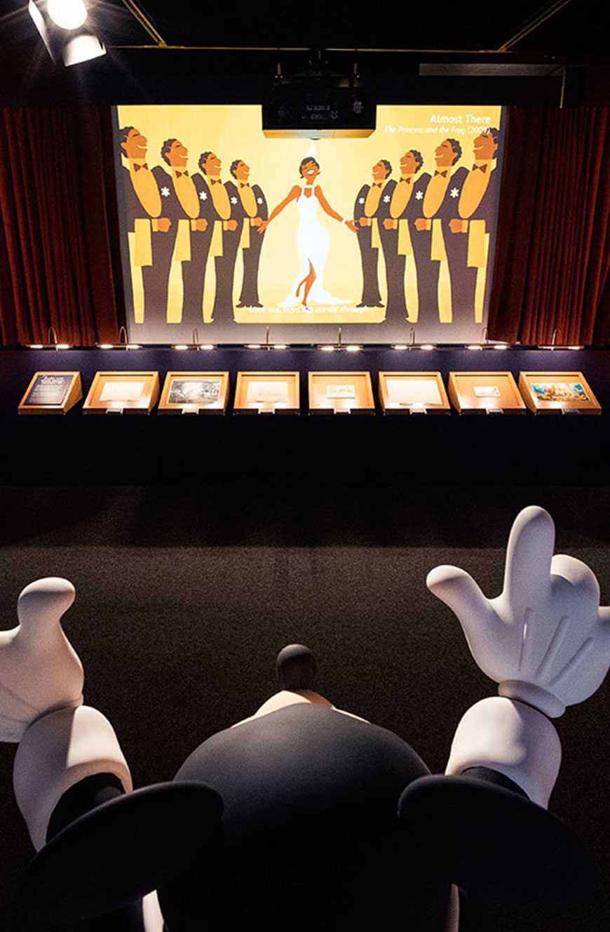 Installationsansicht aus Disney 100 Ausstellung mit Mickey-Figur und Szene aus ‚Küss den Frosch‘ – Medien- und Grafikdesign von cocurio